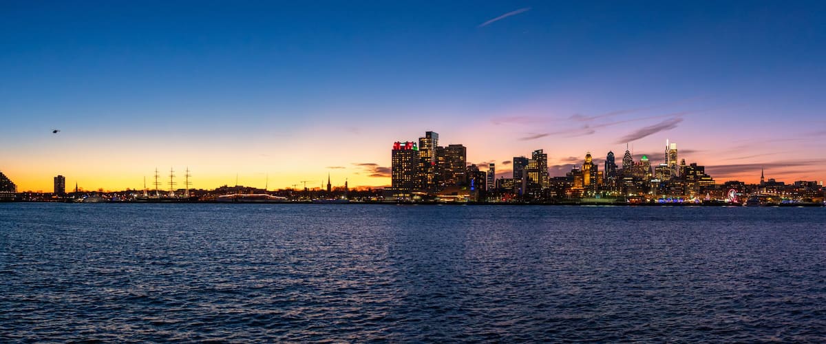 A city skyline at dusk with illuminated buildings and a bridge over water.