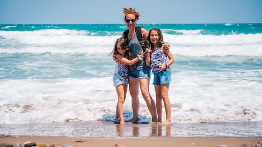 Mother and daughters standing in the sea on a sandy beach laughing.