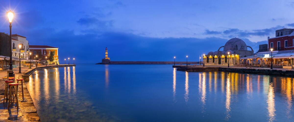 A waterfront with a lighthouse, a mosque, and a row of shops.
