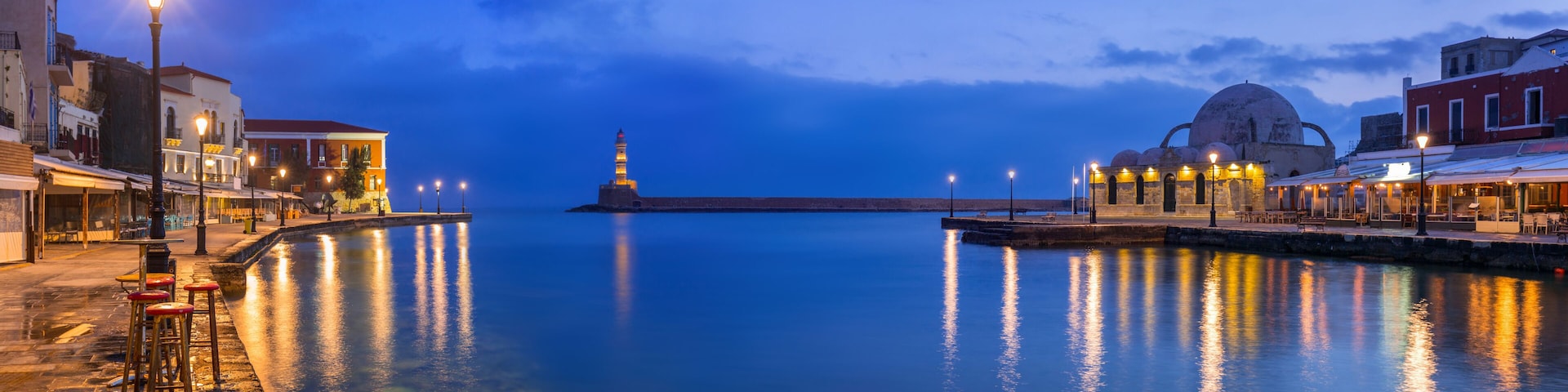 A waterfront with a lighthouse, a mosque, and a row of shops.