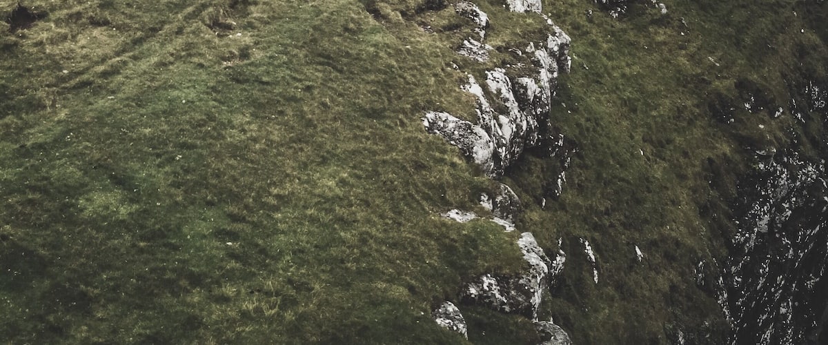 A person hiking on a grassy hillside with rocky outcrops and a large rock formation in the distance.