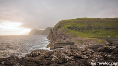 A rugged coastline with rocky shores and green hills in the background.