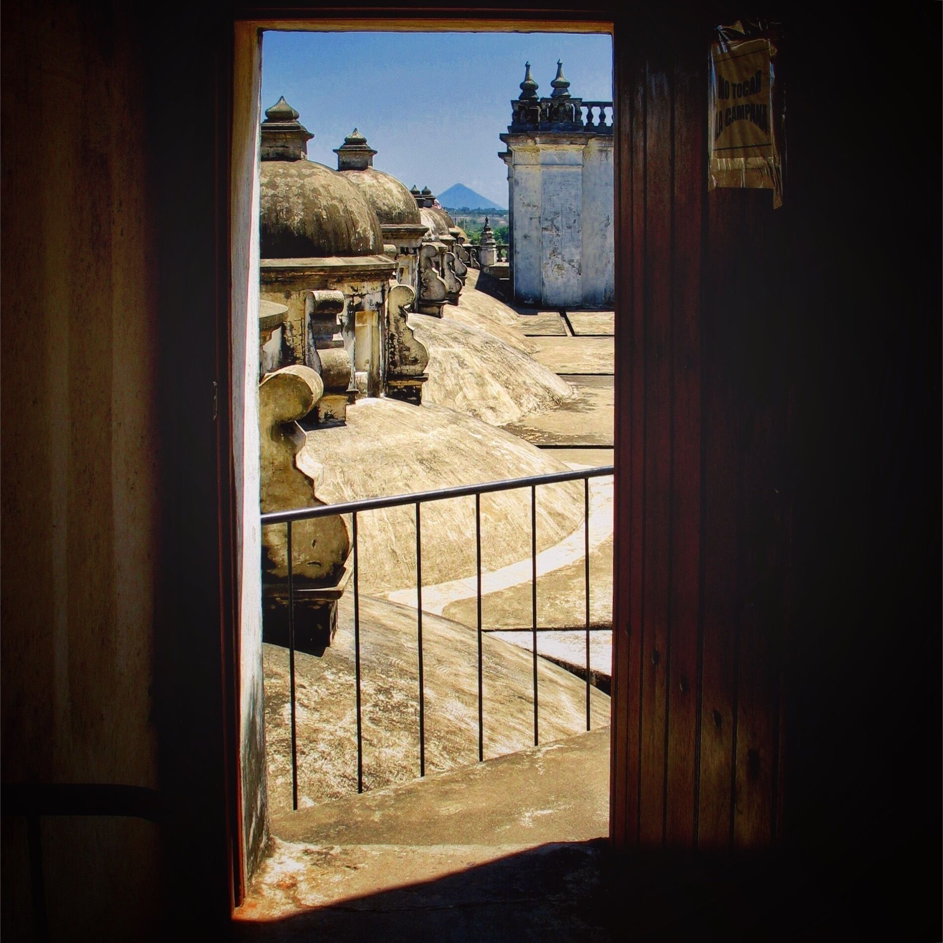 A view through a doorway of a courtyard with stone structures and a mountain in the background.