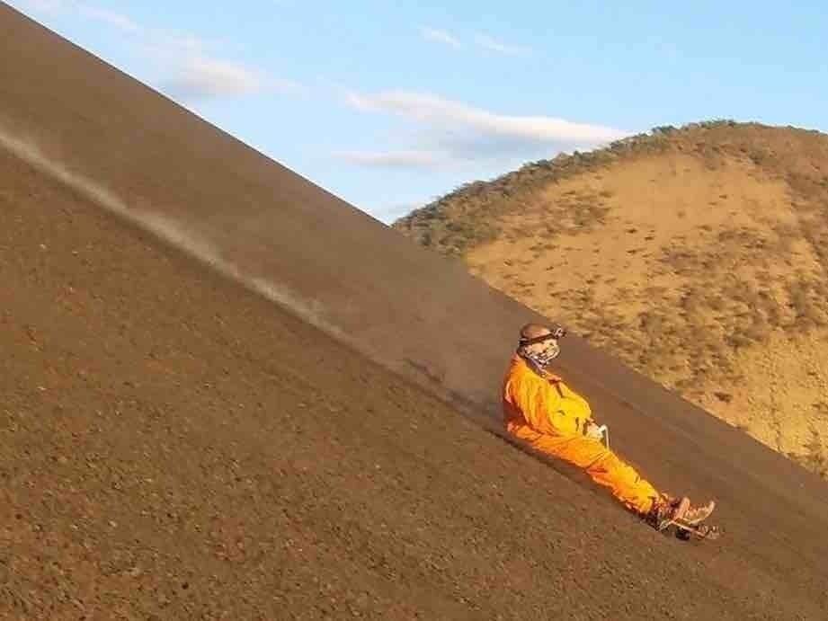 Una persona con equipo de seguridad naranja se desliza por una colina empinada y desolada.