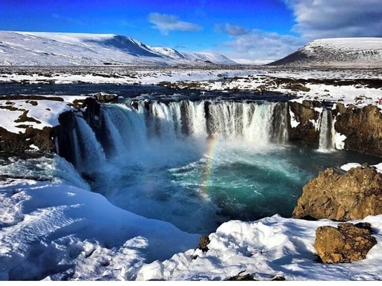 A waterfall in a snowy landscape with a rainbow.