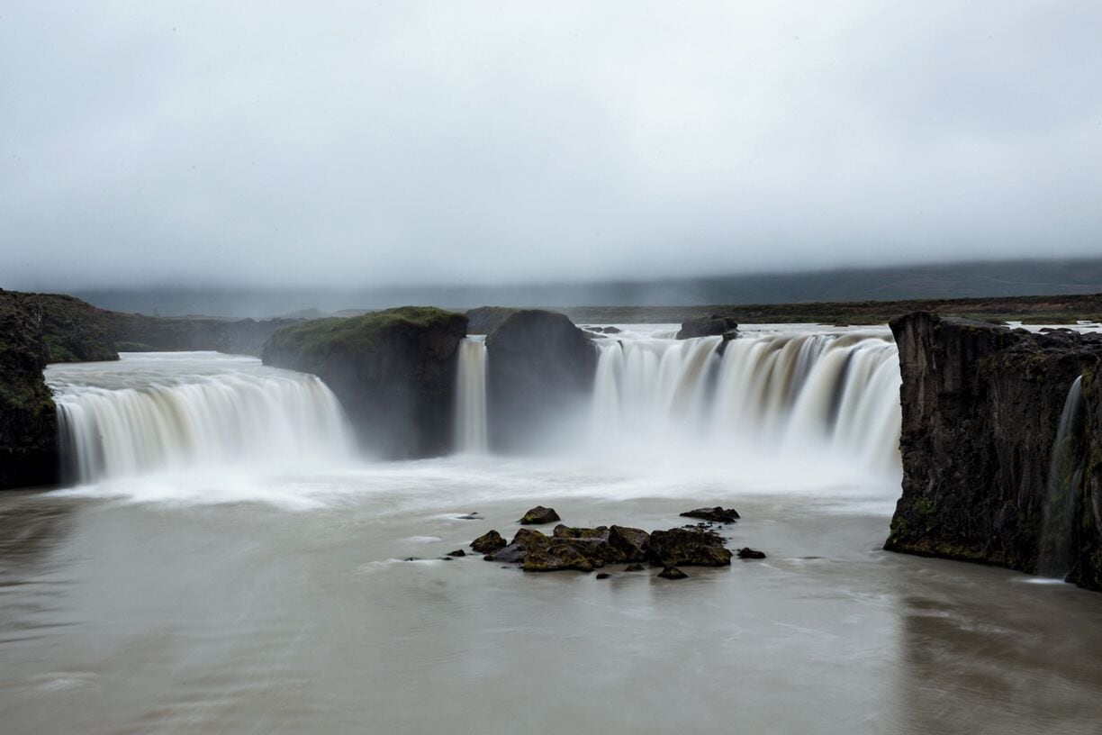 A waterfall cascading over rocks in a misty landscape.