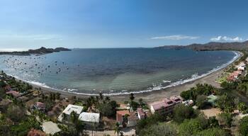 Un pueblo costero con una playa, barcos y una cadena montañosa al fondo.