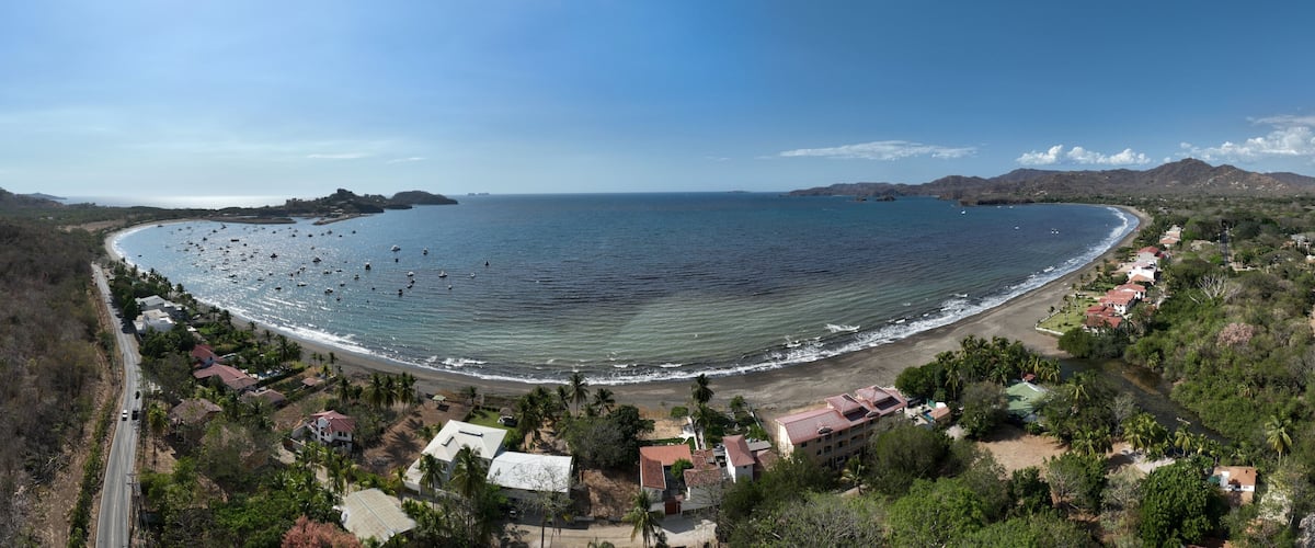 A coastal town with a beach, boats, and a mountain range in the background.