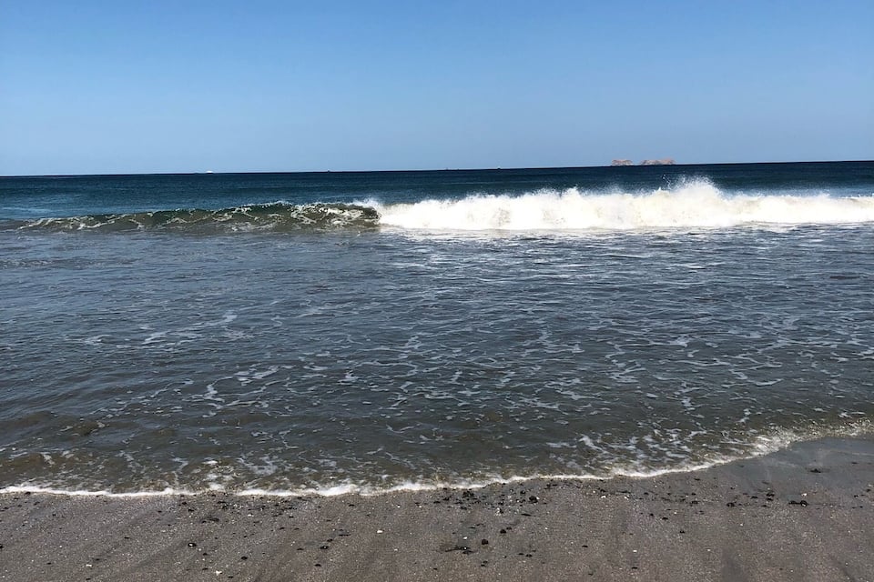 Een strand met golven die op het strand breken en een heldere blauwe lucht.