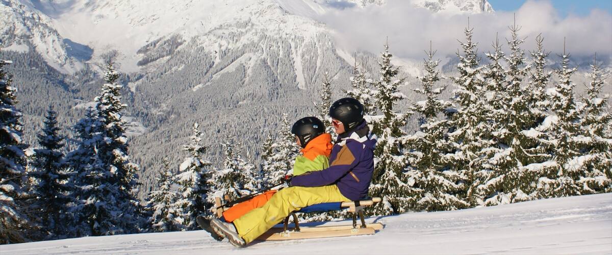A snowy mountain landscape with a ski lift and a person in a colorful jacket sitting on the lift.