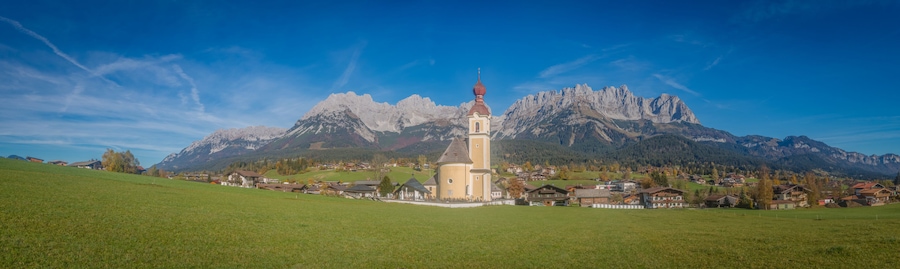Uma igreja com cúpula vermelha e torre do sino, rodeada por uma aldeia e montanhas.