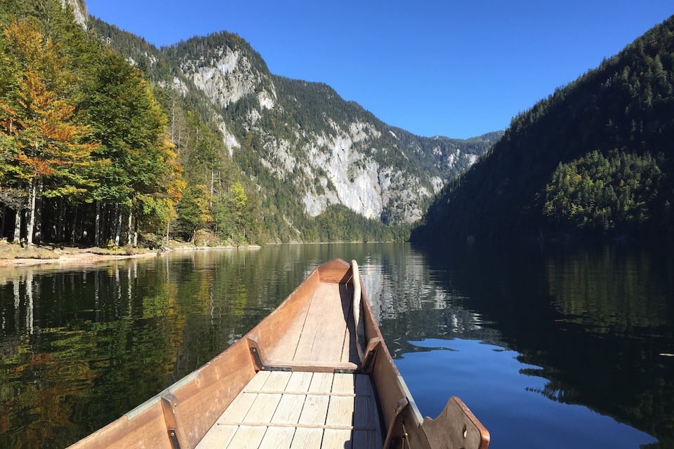 Un bote de madera amarrado en un lago tranquilo rodeado de montañas boscosas.