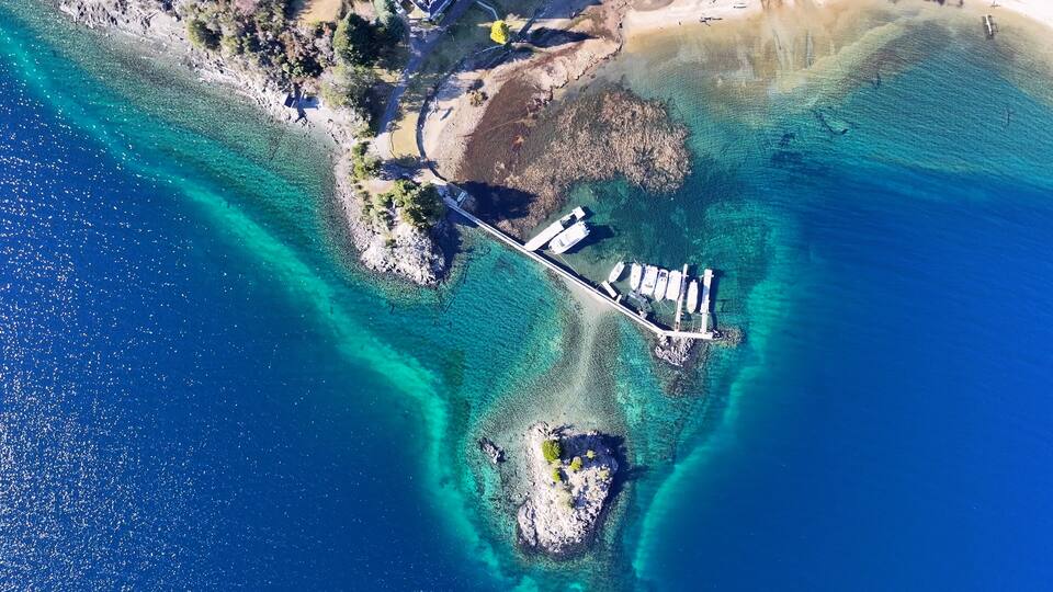 An aerial view of a coastal area with clear blue waters, a rocky shoreline, and a dock with boats.