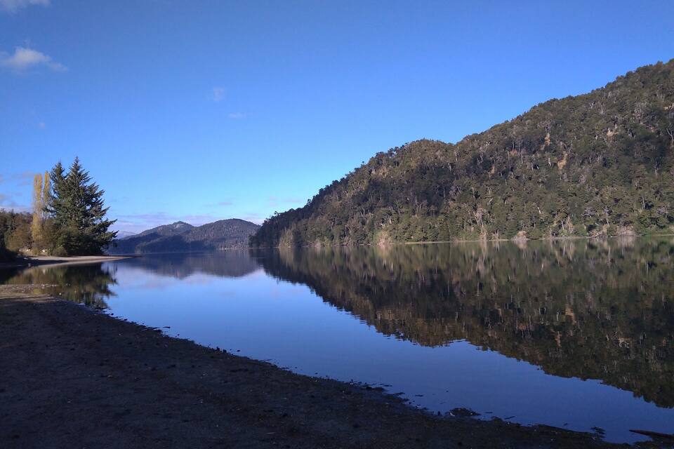 Un lago tranquilo con una montaña boscosa al fondo.