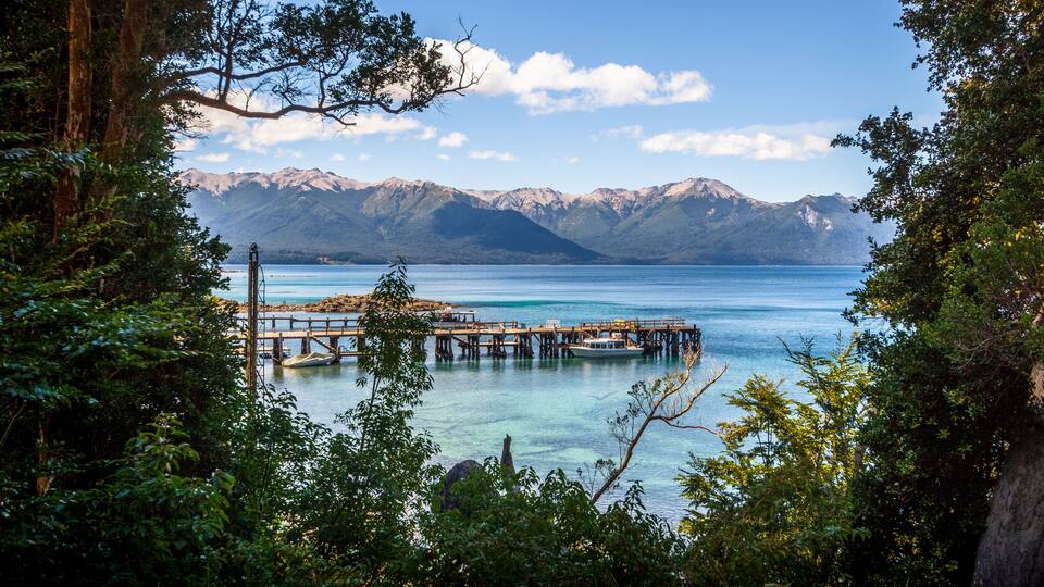 A pier extending into a clear lake with mountains in the background.