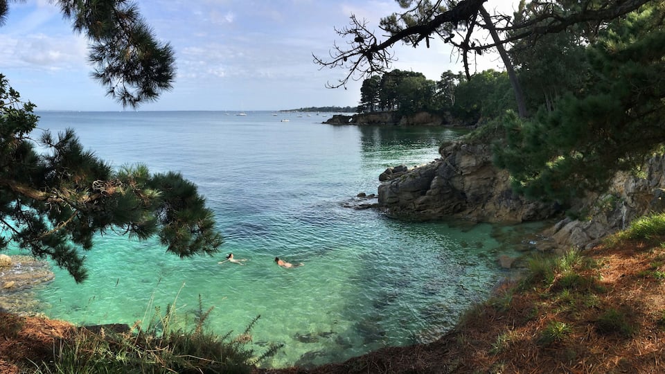 A coastal scene with clear turquoise water, swimmers, and rocky cliffs.