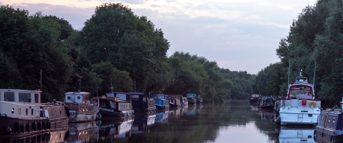 A canal lined with boats and trees reflecting on the water.