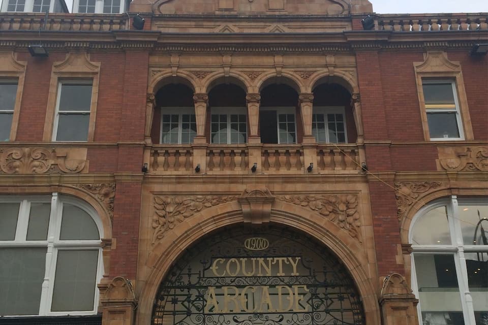 A historic building with ornate architecture, including a large arched entrance labeled "County Arcade" and a clock tower above.