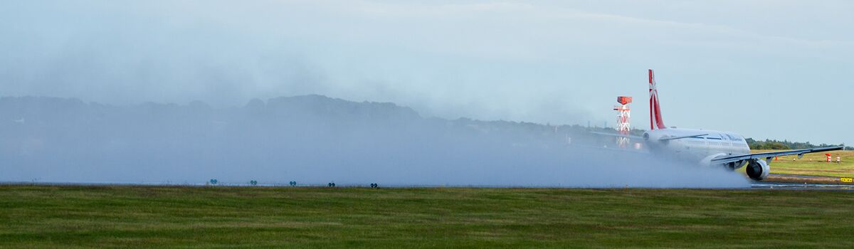 An airplane on a runway with smoke and a distant mountain range.