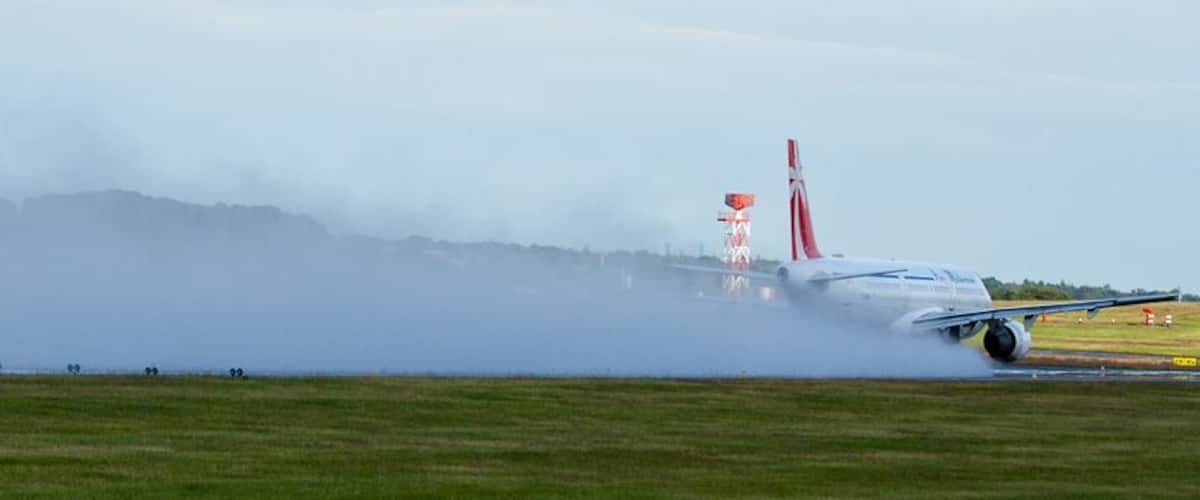 An airplane on a runway with smoke and a distant mountain range.