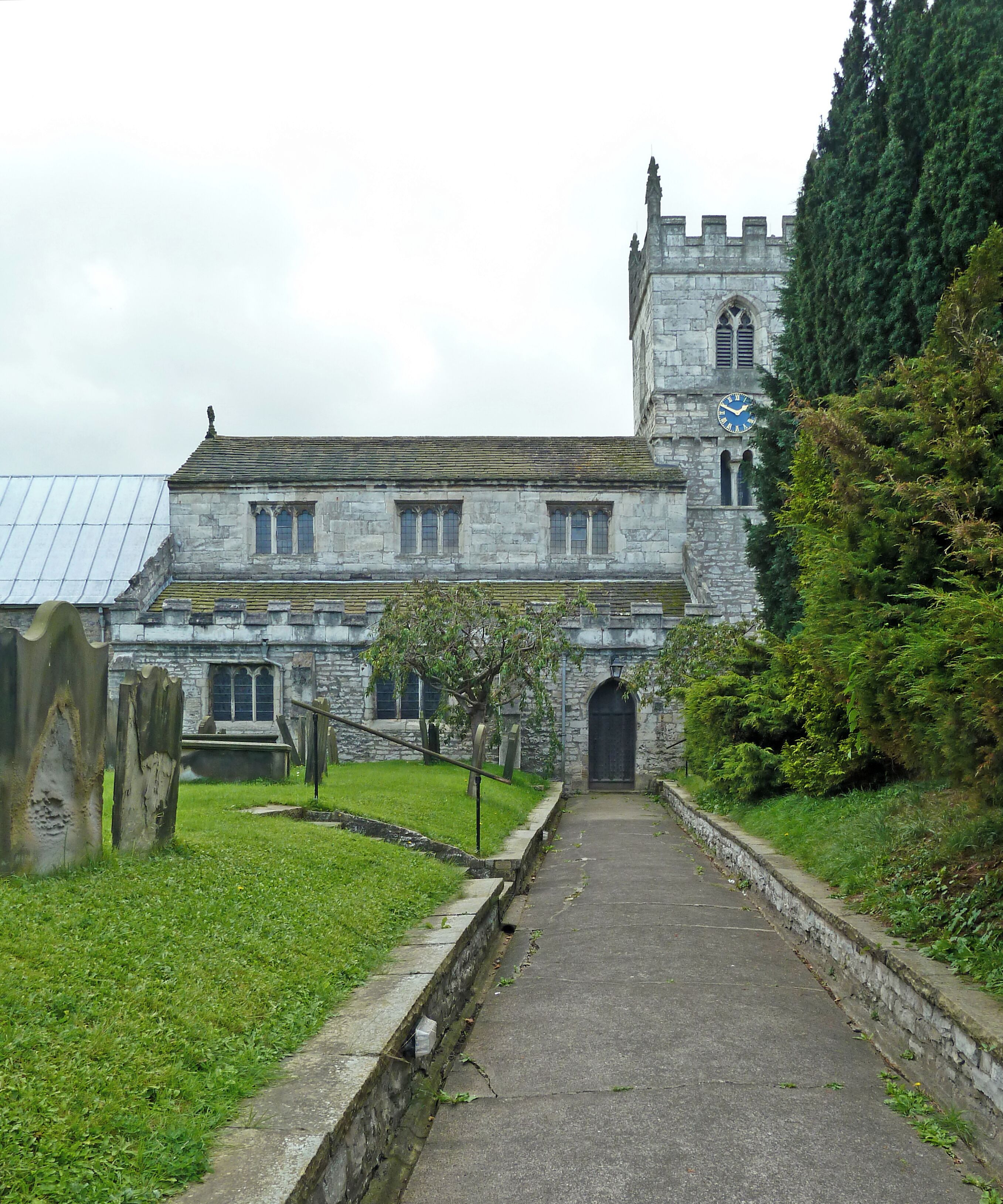 A historic stone building with a clock tower, a pathway leading to the entrance, and a well-maintained lawn.