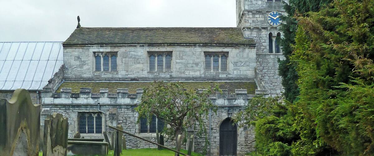 A historic stone building with a clock tower, a pathway leading to the entrance, and a well-maintained lawn.