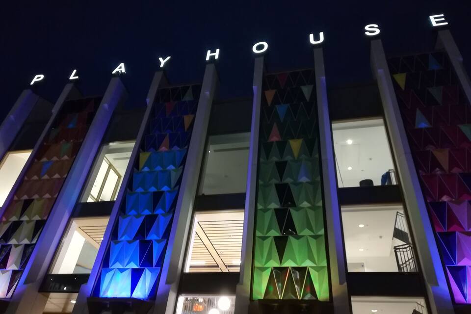 Un edificio con lettere illuminate che formano la parola "PLAYHOUSE" e motivi geometrici colorati sulla facciata.
