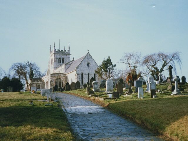 A church with a tower, a cobblestone path, and numerous headstones in a cemetery.