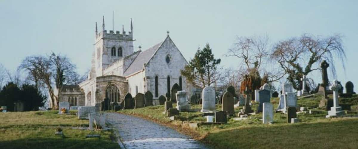 A church with a tower, a cobblestone path, and numerous headstones in a cemetery.