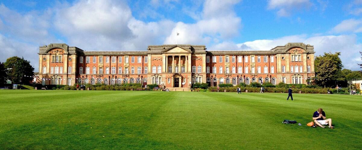 A large red brick building with a central dome and symmetrical windows, surrounded by a well-maintained lawn.