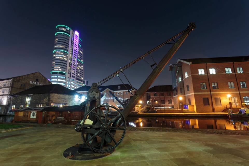 A historical cannon in a public square with a modern illuminated building in the background.