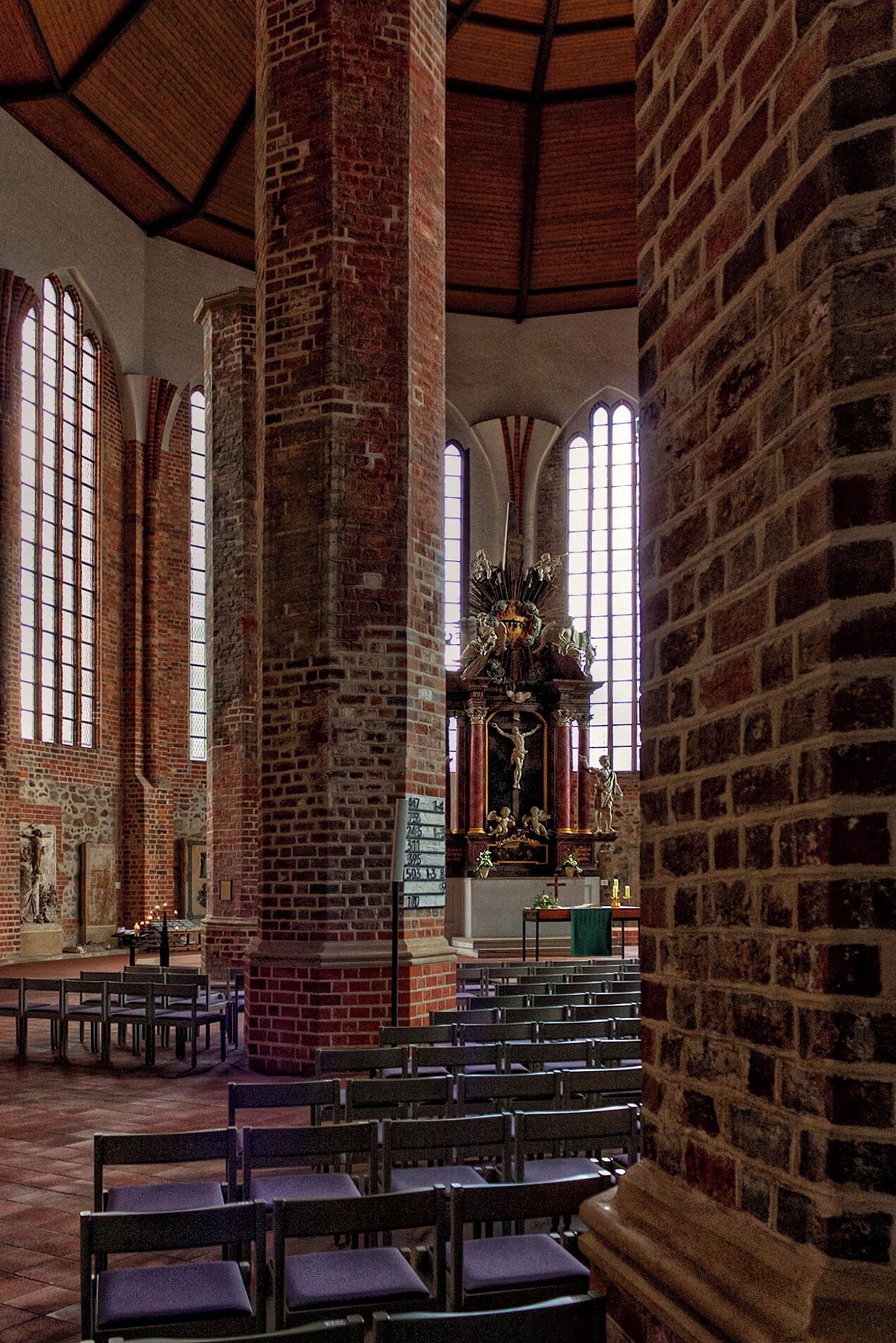 A church interior with brick columns, arched windows, and a central altar with a statue.