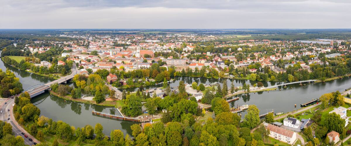 A river flowing through a town with a bridge, surrounded by greenery and buildings.