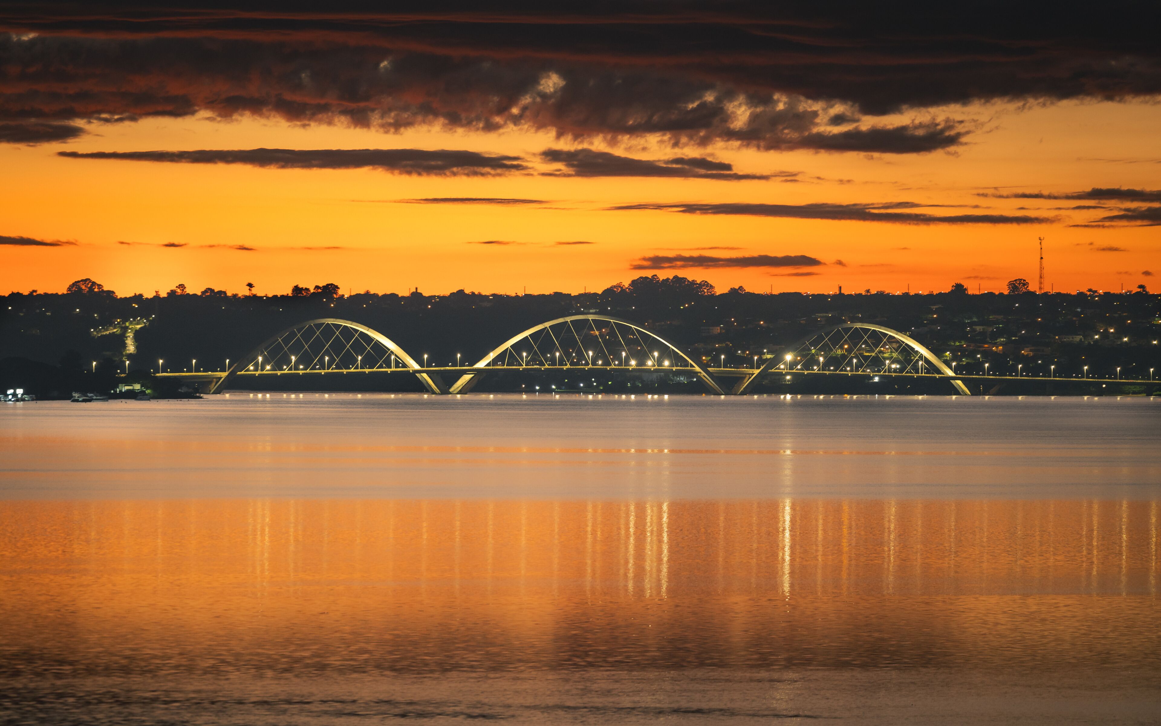 Un coucher de soleil sur une rivière, avec un pont orné de trois arches.