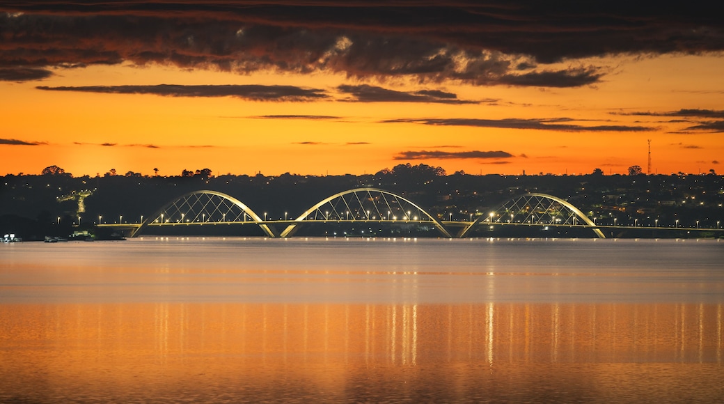 Un coucher de soleil sur une rivière, avec un pont orné de trois arches.