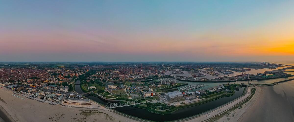 An aerial view of a coastal city with a beach, a river, and a bridge.