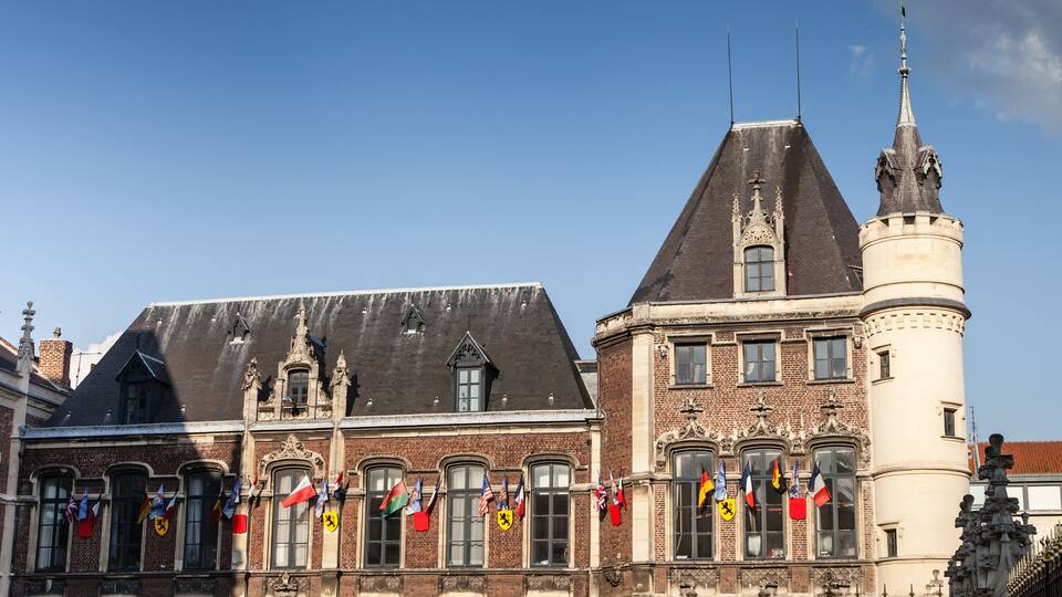 A historic building with multiple flags, a pointed roof, and a tower with a spire.