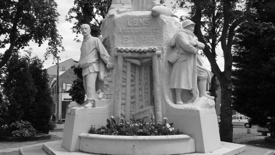 A monument with figures, surrounded by trees and a paved area.