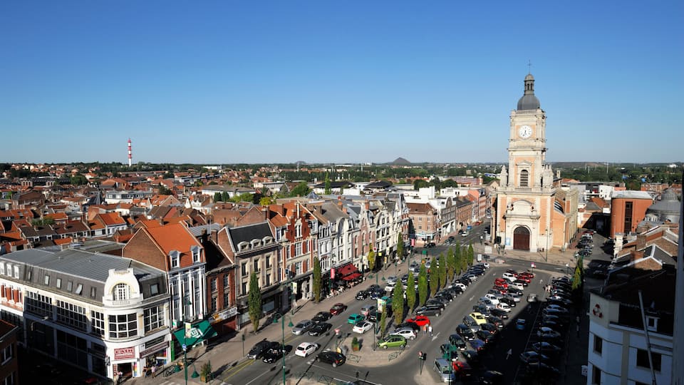 A cityscape with a prominent clock tower, historic buildings, and a clear blue sky.