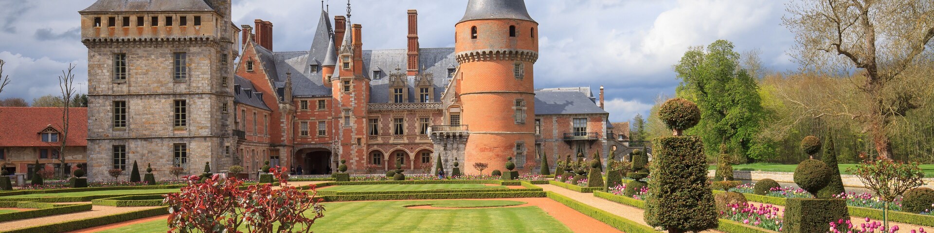 Um castelo histórico com torres e um jardim bem cuidado com tulipas.