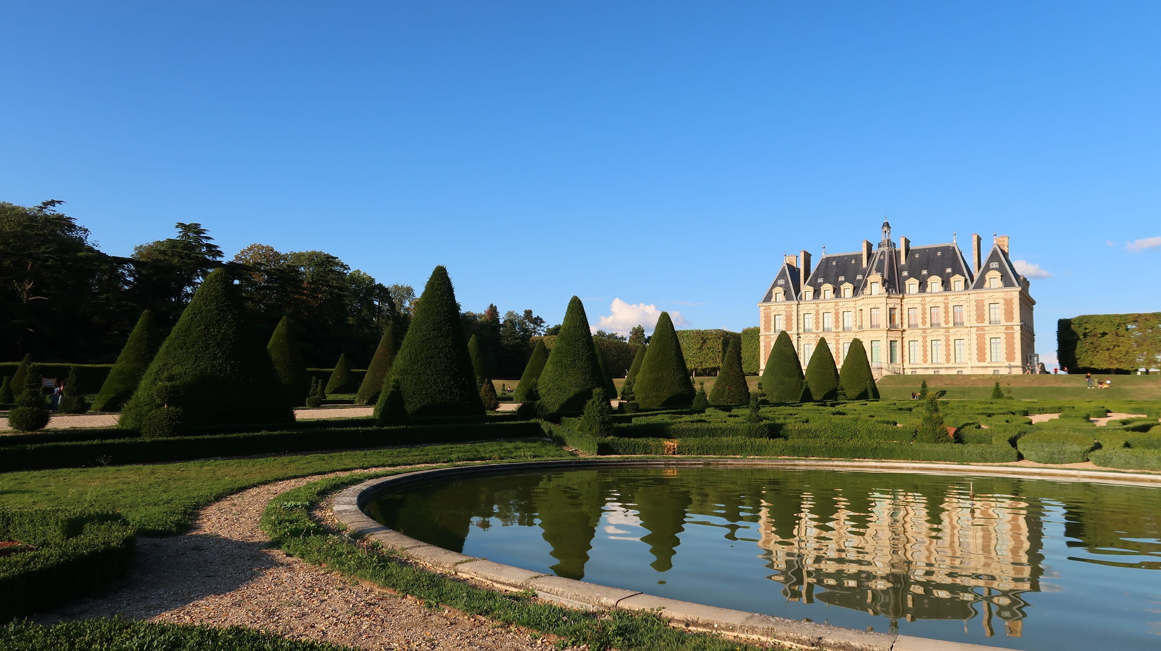 Domaine du parc de Sceaux dans les Hauts-de-Seine, paysage avec un château se reflétant dans un bassin et une rangée d'ifs taillés dans un jardin à la française (France)