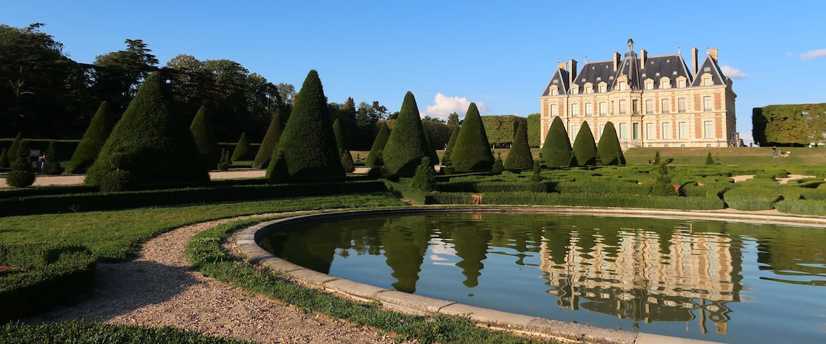 A formal garden with a reflective pond, neatly trimmed hedges, and a large historic building.