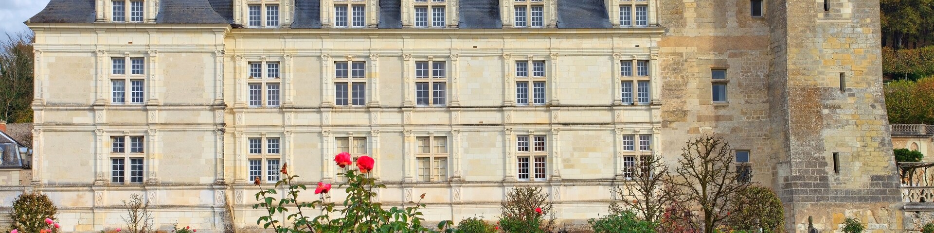 Um castelo histórico com um amplo jardim, com flores vibrantes e sebes bem aparadas.