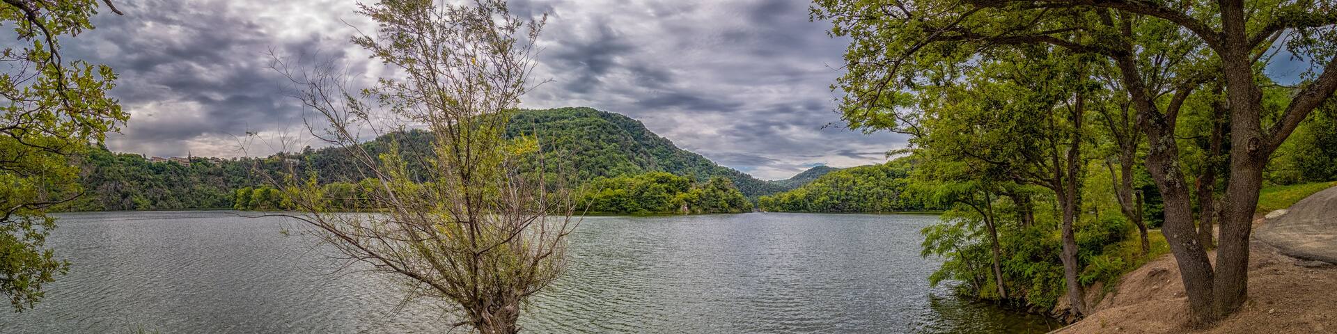 A lake surrounded by hills and trees under a cloudy sky.