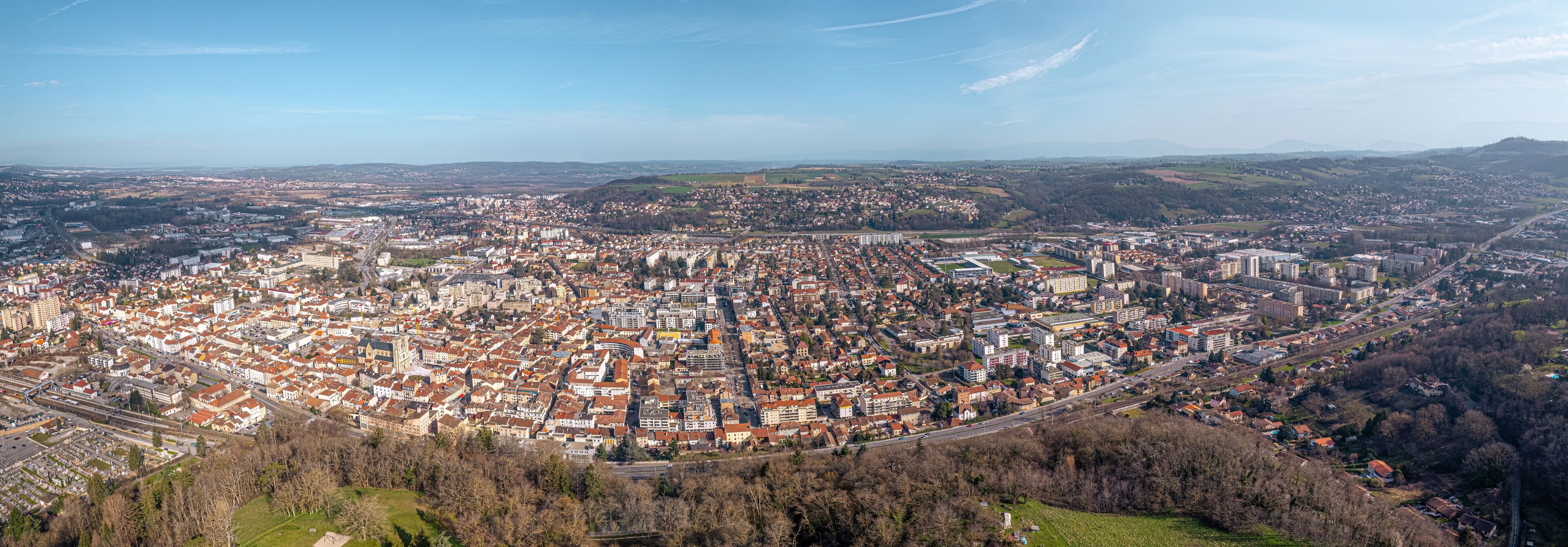 An aerial view of a densely populated city with a mix of historic and modern architecture, surrounded by rolling hills and a clear sky.