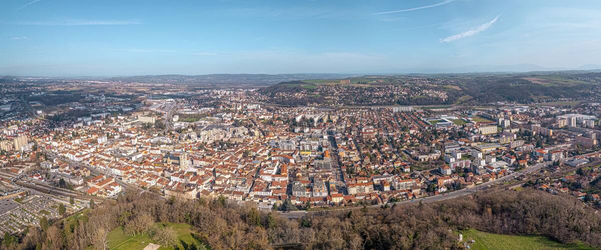 An aerial view of a densely populated city with a mix of historic and modern architecture, surrounded by rolling hills and a clear sky.