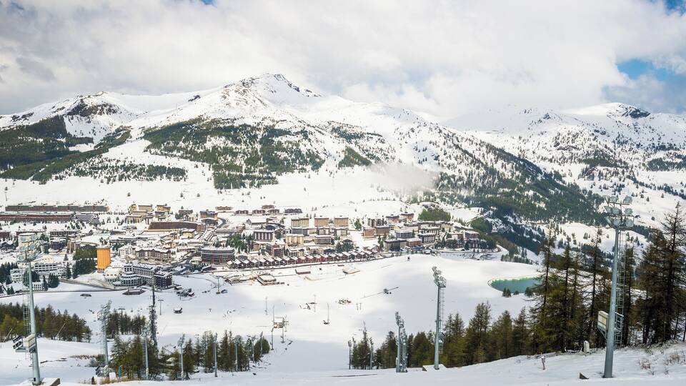 A snow-covered mountain town with buildings, ski slopes, and a lake.