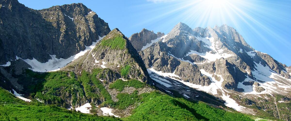 A mountain range with snow patches and lush green vegetation.