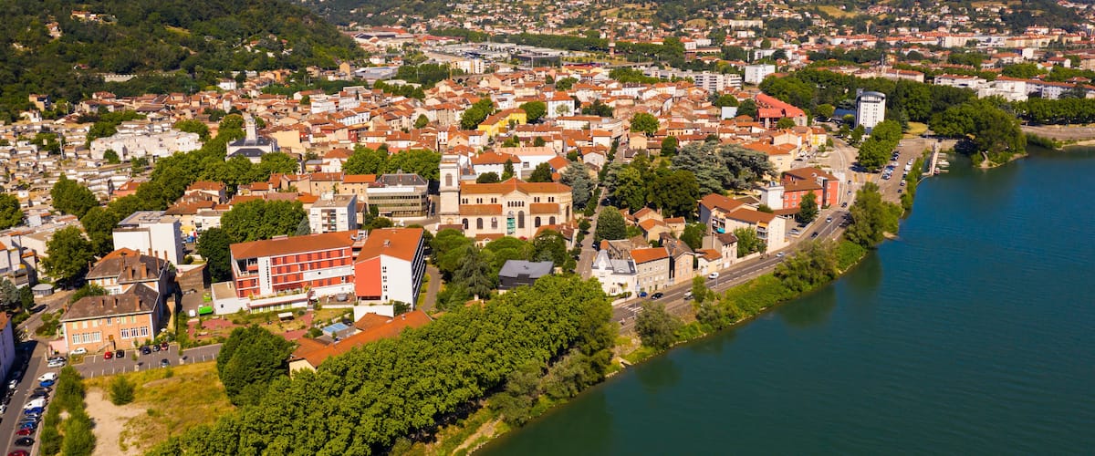 A river winding through a town with red-roofed buildings and a mountainous backdrop.