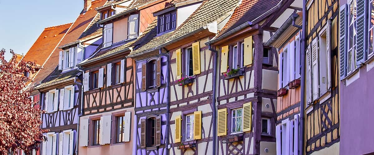 A row of half-timbered houses with colorful shutters and a tree with autumn leaves.